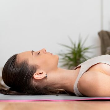 Frau liegt entspannt auf dem Rücken und führt eine progressive Muskelrelaxation nach Jacobsen durch